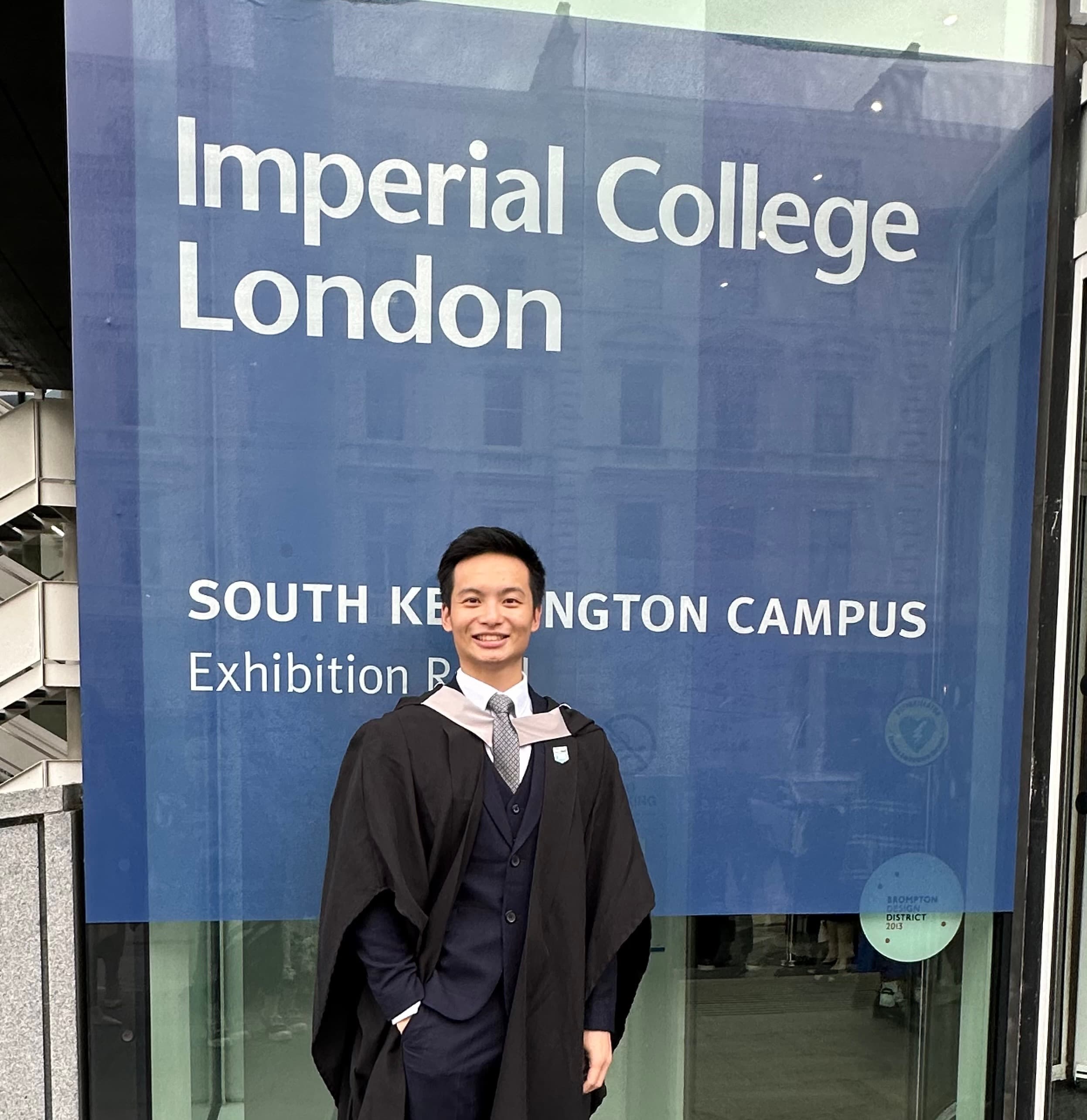 Vincent in cap and gown outside the Imperial College London South Kensington campus sign